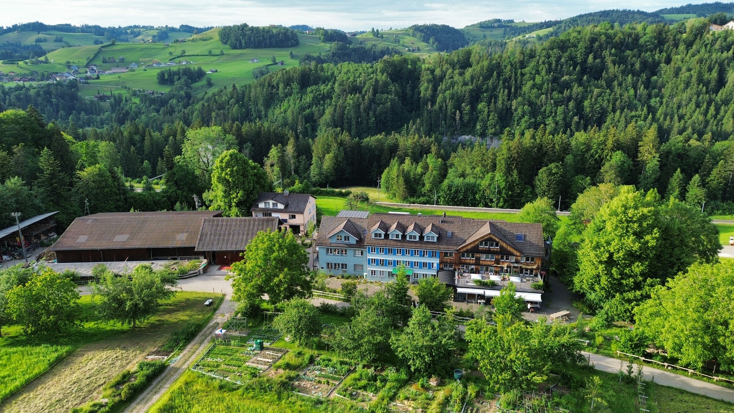 Wohnhaus, Bruggenhof und Pflanzgärten von oben, dahinter die Hügel des Neckertals